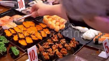 亚洲美食，美食理念.. 接近。 手拿钳子在街上的夜市上选择寿司。